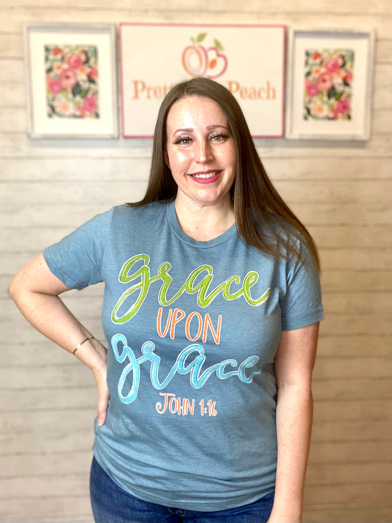 Model wearing our grace upon grace tee. The tee is light blue with lettering on it of green, orange, and bright blue.