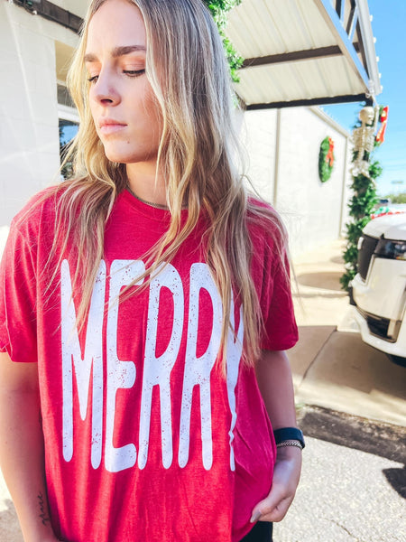 Model wearing our red merry tee. The tee is short sleeve and has the word MERRY written largely across it.