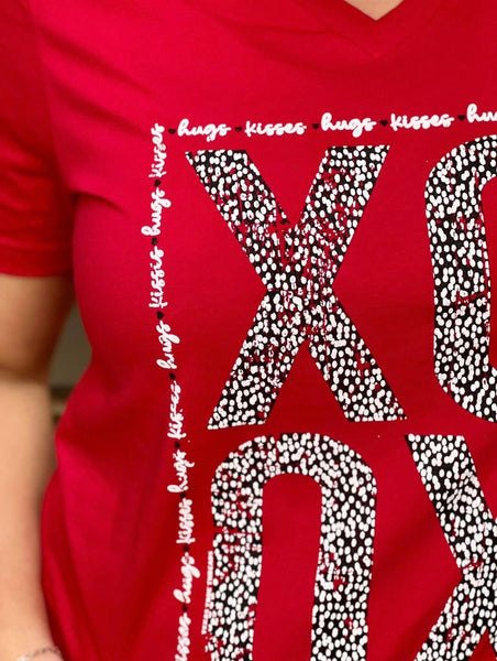 Model wearing our red xoxo tee. The tee is short sleeve and bright red with v-neck. The letters xoxo are in bold with black and white leopard print making them. hugs and kisses is written in cursive around the bold letters making a rectangle border.