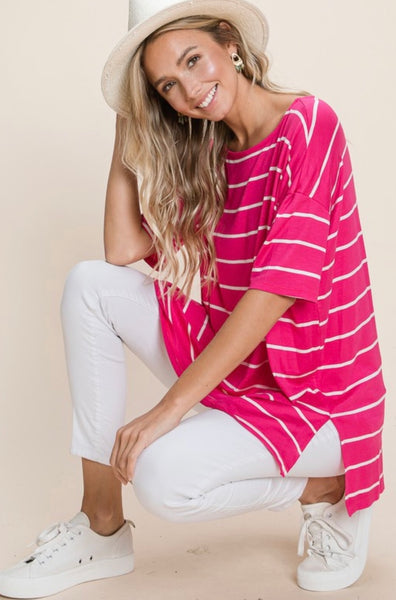 Model wearing our Fuchsia Oversized Striped Tunic. The top is elbow length and oversized. The top is fuchsia with white stripes horizontally. Model pairs the top with white jeans, sneakers, and hat.