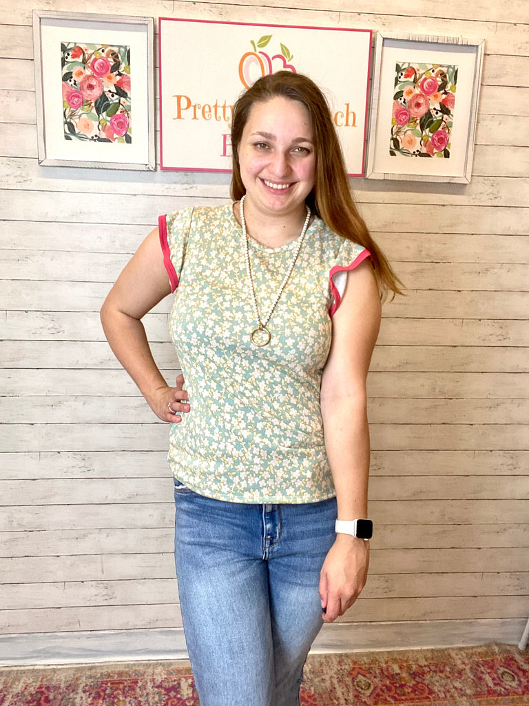 Model wearing our Mint & Ivory Floral Ruffle Sleeve Top. The top is short sleeve and has ruffle sleeves with a pink trim. The bodice is mint with ivory floral pattern. 