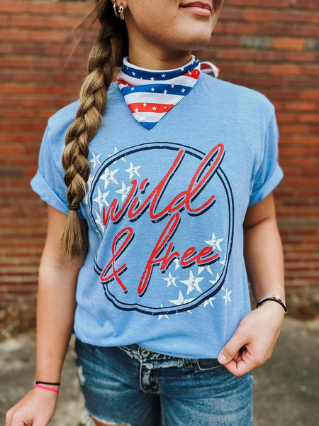 Model wearing our Blue Wild & Free Tee. The top is short sleeve and has a scoop neckline. The top has a dark blue circle with wild & free written in red cursive and white stars on the top left and bottom right corners.  