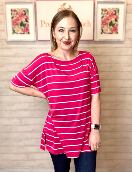 Model wearing our Fuchsia Oversized Striped Tunic. The top is elbow length and oversized. The top is fuchsia with white stripes horizontally. Model pairs the top with dark denim jeans.
