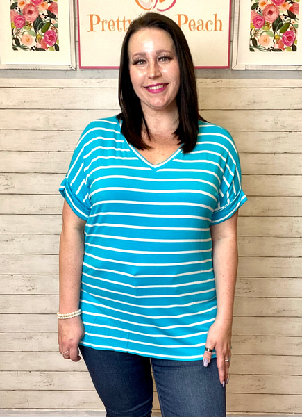 Model wearing our Deal of the Day Blue Striped Top. The top is short sleeve and is blue with white stripes. The top has a v neckline, folded sleeves, and a split on the sides with the top longer in the back than the front.