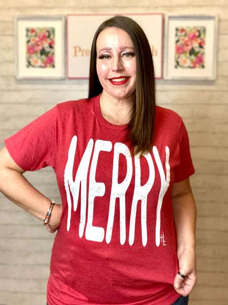 Model wearing our red merry tee. The tee is short sleeve and has the word MERRY written largely across it.