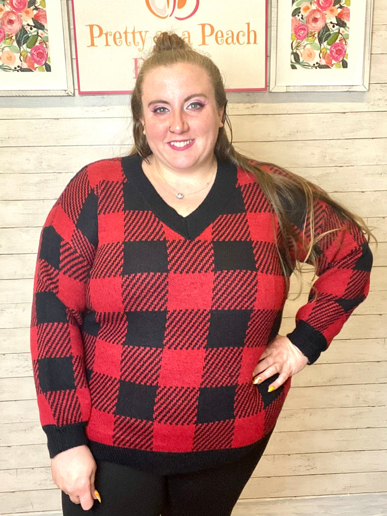 Model wearing about Black & Red Buffalo Plaid Sweater. The sweater is V-neck and has black trim on the neckline, bottom hem, and wrist cuffs.