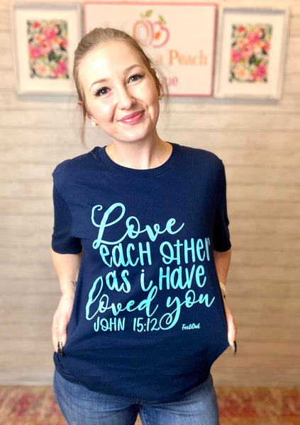 Model wearing our love each other tee. The tee is short sleeve and navy with light blue lettering. The words Love, loved love, and John are written in cursive the rest is more whimsical print. 