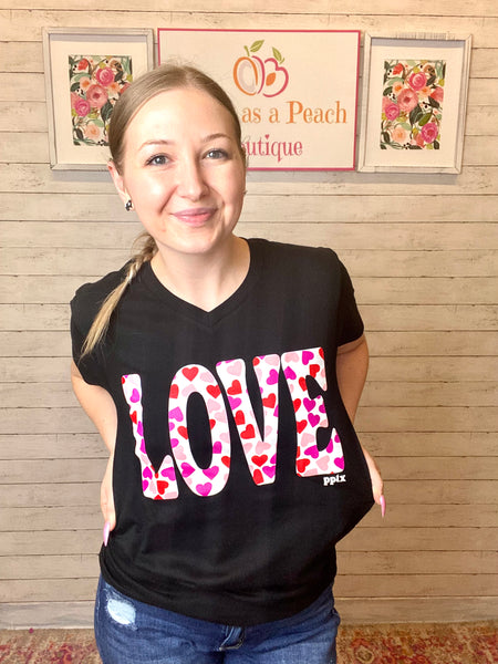 Model wearing our love heart tee. The tee is short sleeve and black with LOVE written in bold white with red and pink hearts inside. The tee is a subtle v-neck and can be paired with so many things.