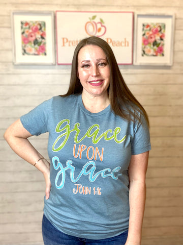 Model wearing our grace upon grace tee. The tee is light blue with lettering on it of green, orange, and bright blue. 