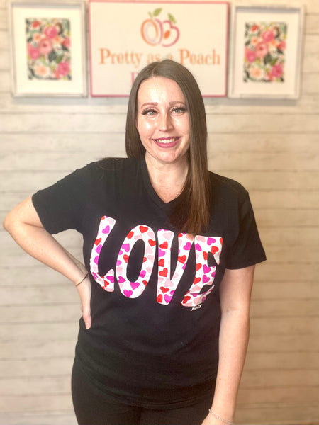 Model wearing our love heart tee. The tee is short sleeve and black with LOVE written in bold white with red and pink hearts inside. The tee is a subtle v-neck and can be paired with so many things.