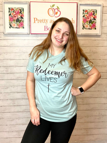 Model wearing our my redeemer lives tee. The tee is light blue and short sleeve with the writing on the chest and a cross at the bottom.