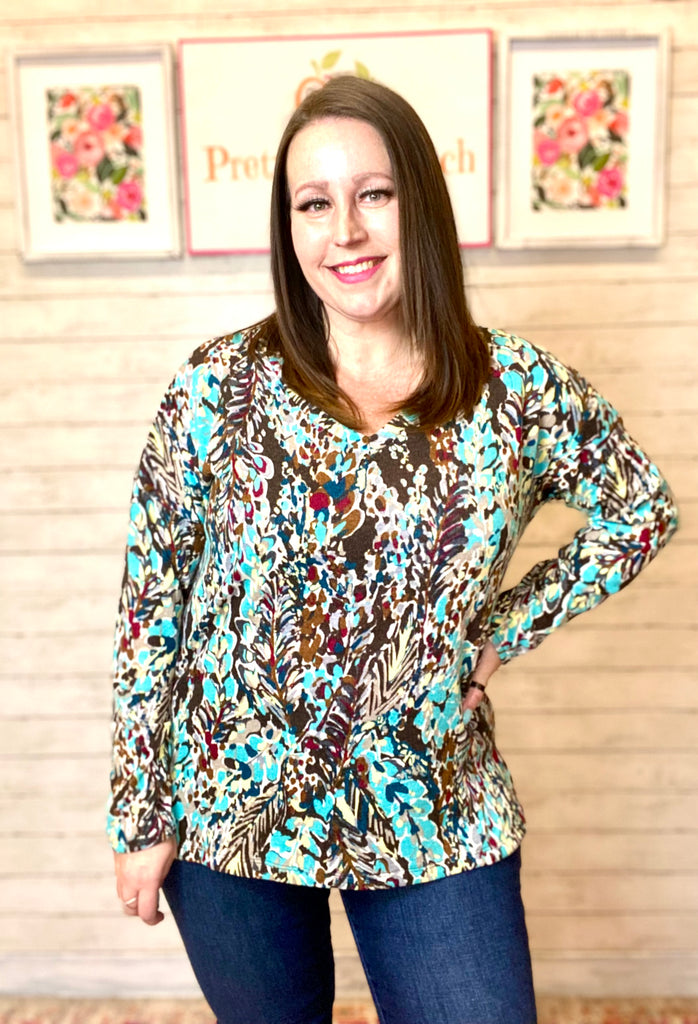Model wearing our Brown & Teal Floral Contrast Top. The top is long sleeve and has a print with brown, teal, maroon, gray, and white. Model pairs the top with dark denim.
