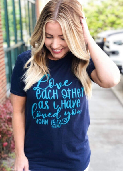 Model wearing our love each other tee. The tee is short sleeve and navy with light blue lettering. The words Love, loved love, and John are written in cursive the rest is more whimsical print.