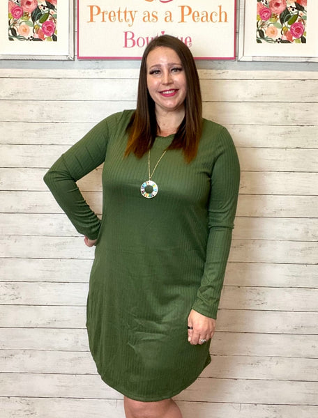 Model wearing our olive ribbed dress. The dress is long sleeve and hits just above the knee. Model pairs the dress with a long gold necklace.  